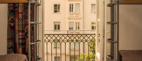 Un pasillo estrecho con literas a ambos lados, que conduce a un balcón abierto con vistas a un edificio con balcones.
