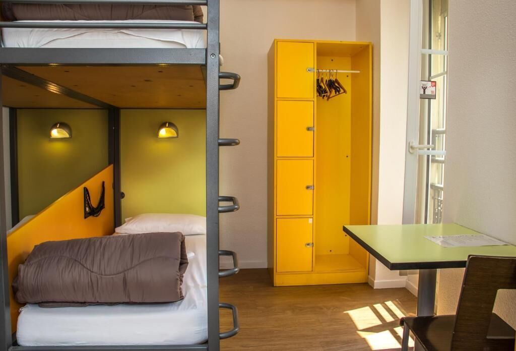 Un dormitorio con literas, un armario amarillo, un escritorio y una ventana.