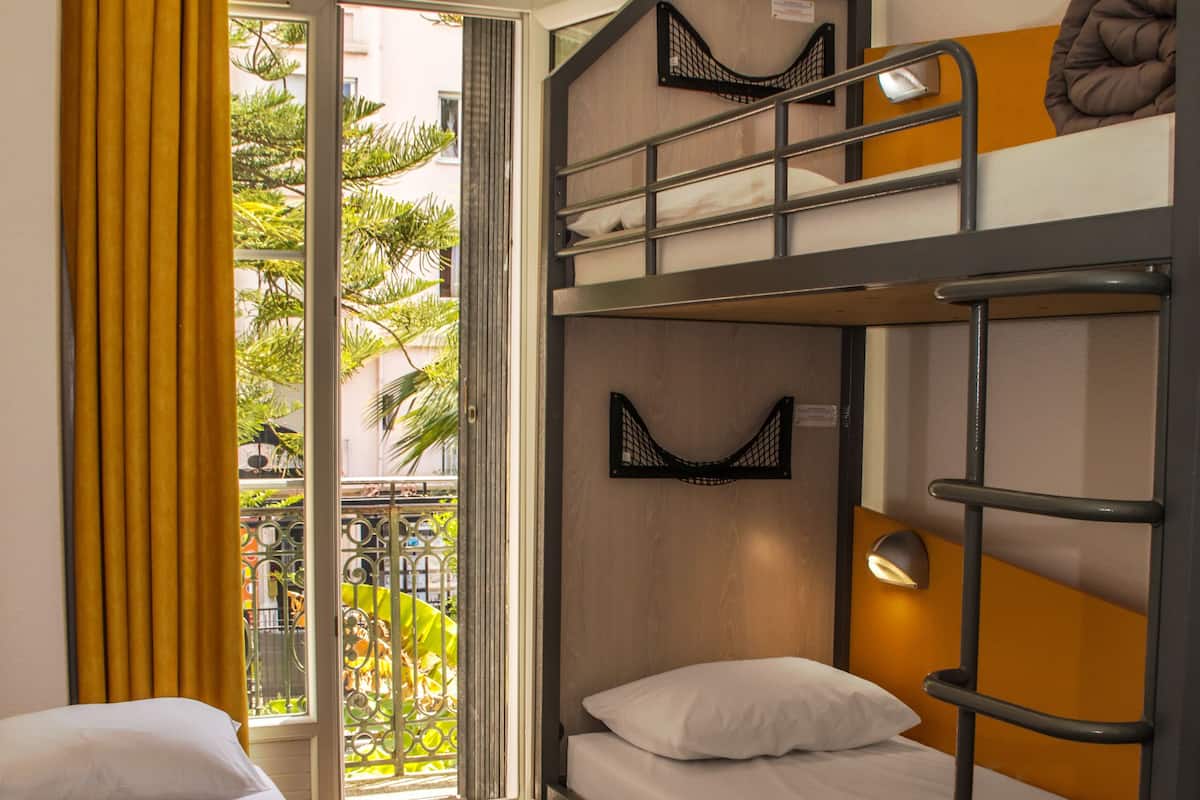 A bunk bed room with a view of a balcony and a window with yellow curtains.