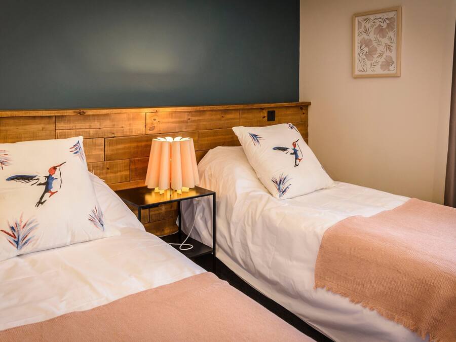 Two single beds with matching headboards and pillows, a bedside table with a lamp, and a framed floral artwork on the wall.