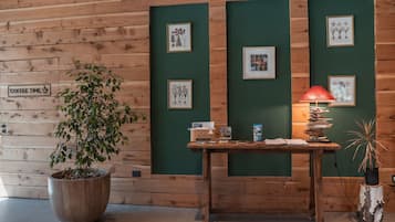 A wooden wall with framed botanical illustrations, a coffee sign, and a table with a lamp and books.