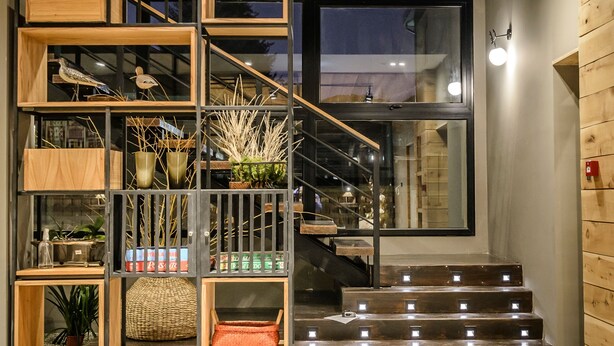 Un interior moderno con una escalera de madera, barandales de metal y diversos objetos decorativos, como plantas y cestas.