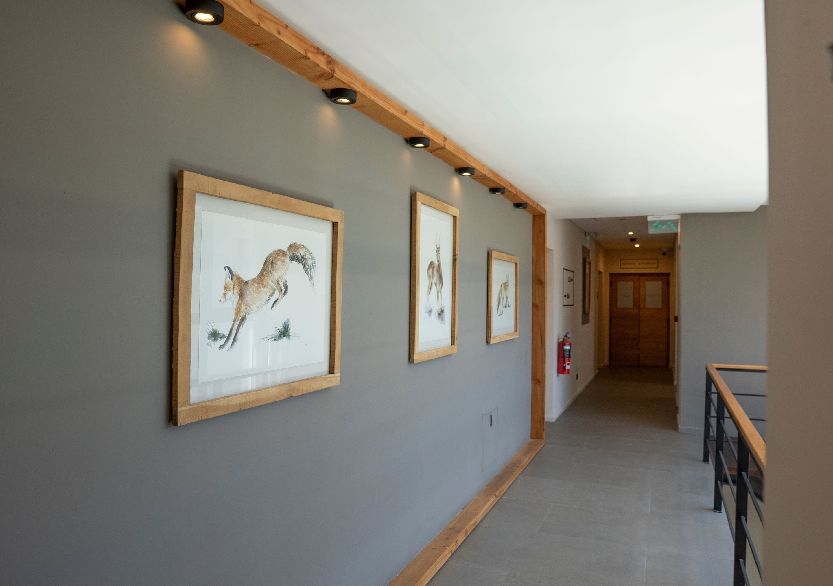 A hallway with framed artwork on the walls, wooden beams, and a staircase with a wooden railing.