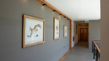 A hallway with framed artwork on the walls, wooden beams, and a staircase with a wooden railing.