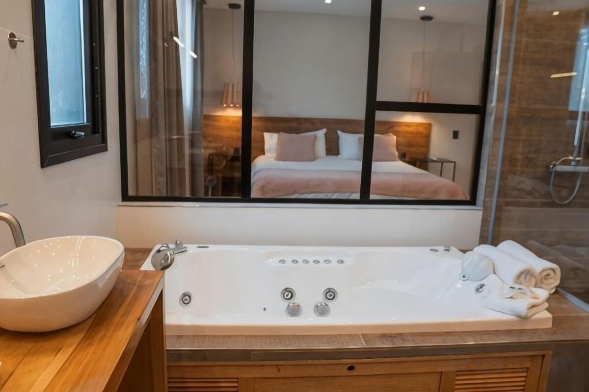 Ein Badezimmer mit einer großen Badewanne, einem Waschbecken und einem Spiegel, der einen Blick auf ein Schlafzimmer bietet.