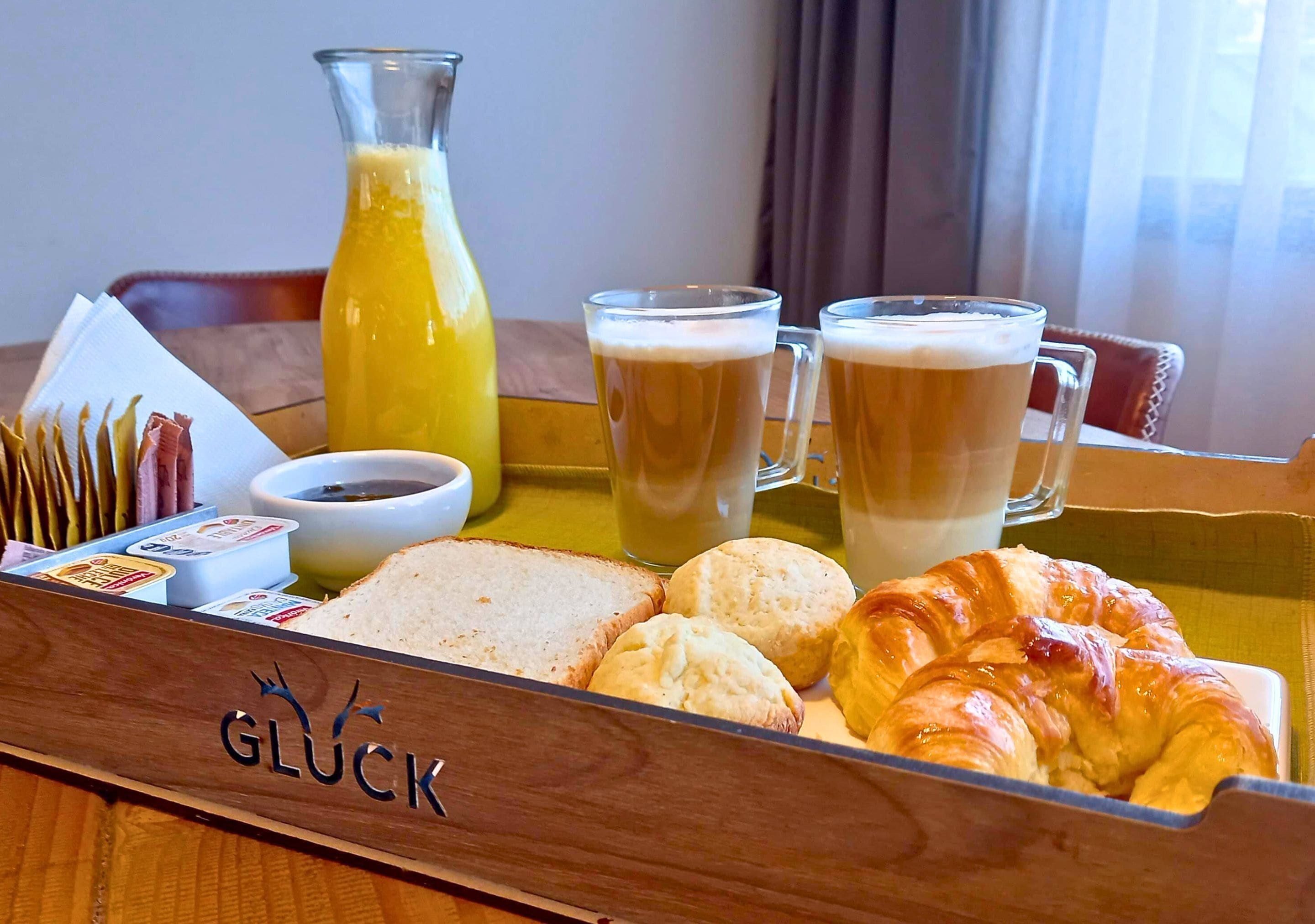 Ett frukostbricka med bröd, croissanter, juice och två kaffemuggar.