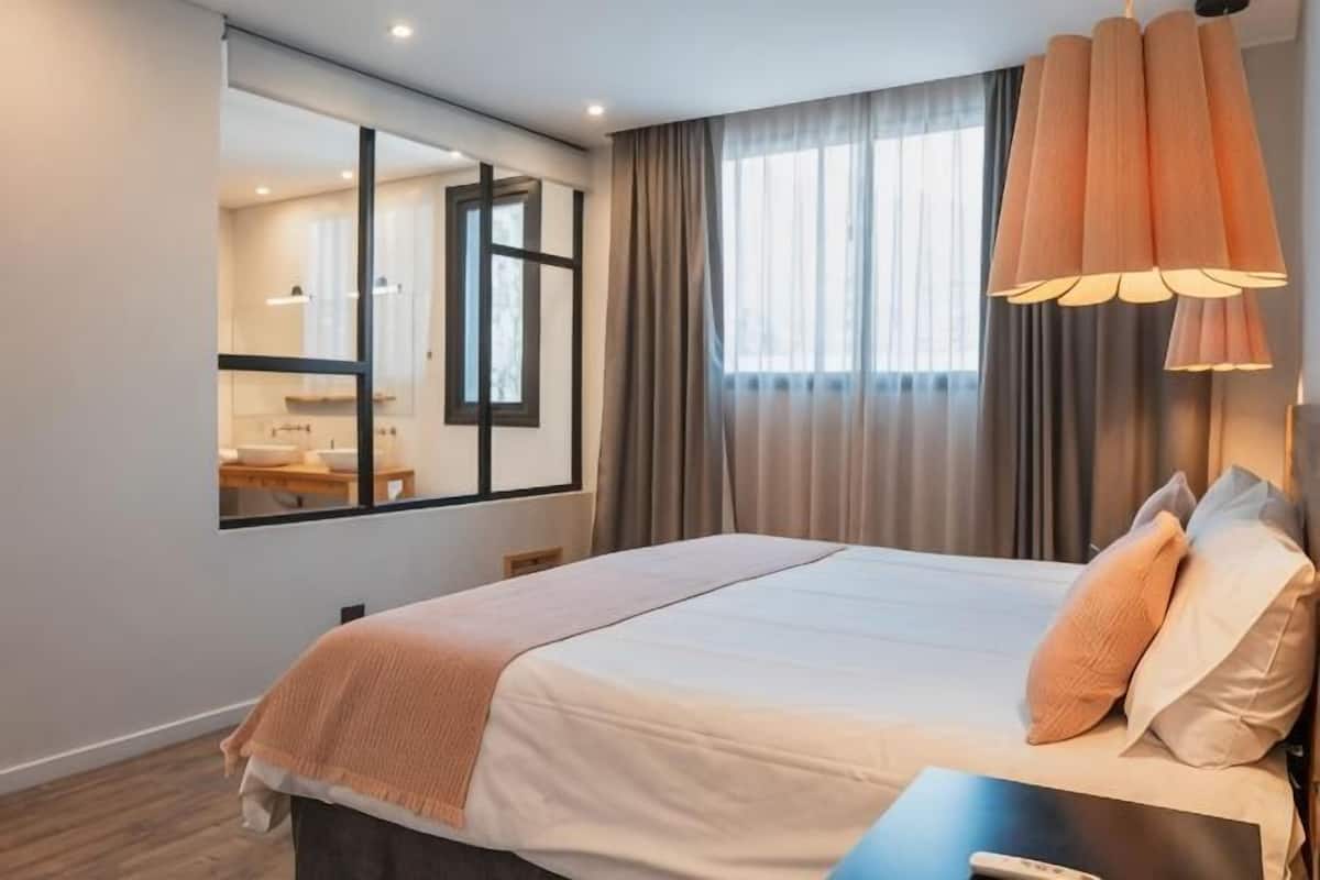 Ett hotellrum med en stor säng, ett skrivbord, en spegel och ett fönster med gardiner.