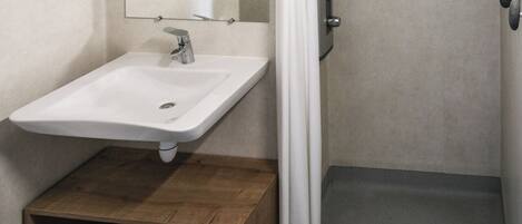 Un baño moderno con lavamanos, espejo, ducha y un mueble de madera.
