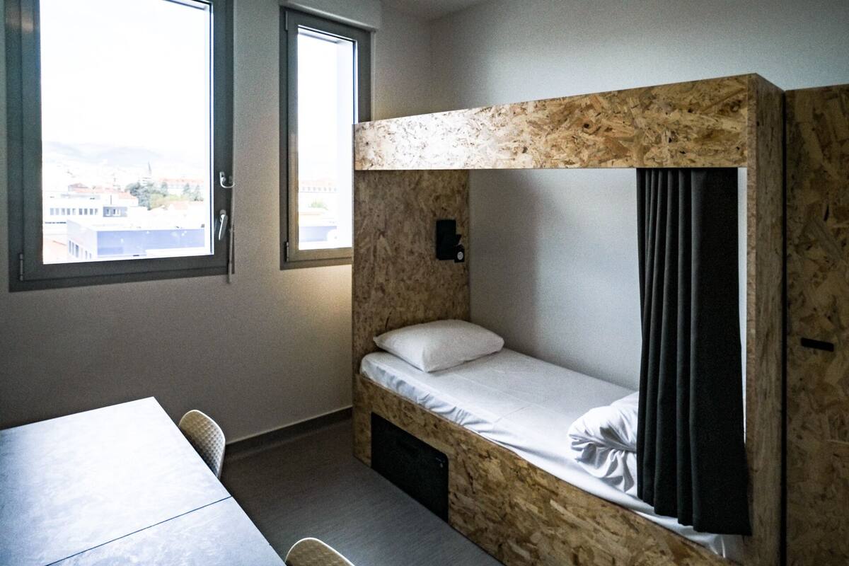 A bunk bed with a wooden headboard, a single bed, and a small table with a chair.