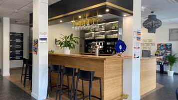 Zona de bar moderna con mostrador de madera, taburetes, una planta en maceta y una lámpara colgante decorativa.