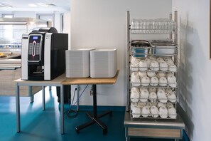 A coffee machine, stacks of plates, and a rack of teapots in a kitchen area. - Auberge de jeunesse HI Clermont-Ferrand (Clermont-Ferrand)