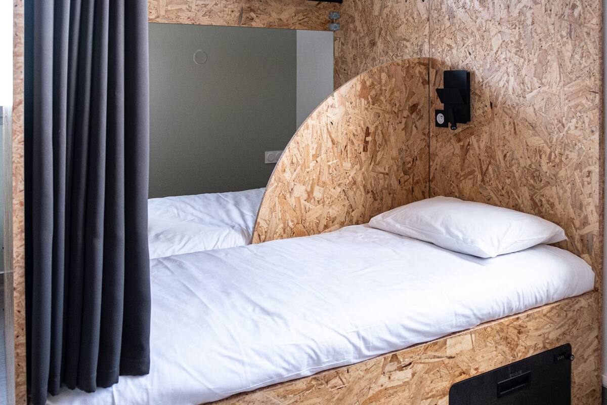 A single bed with white bedding in a room with wooden panel walls and a black switchboard.