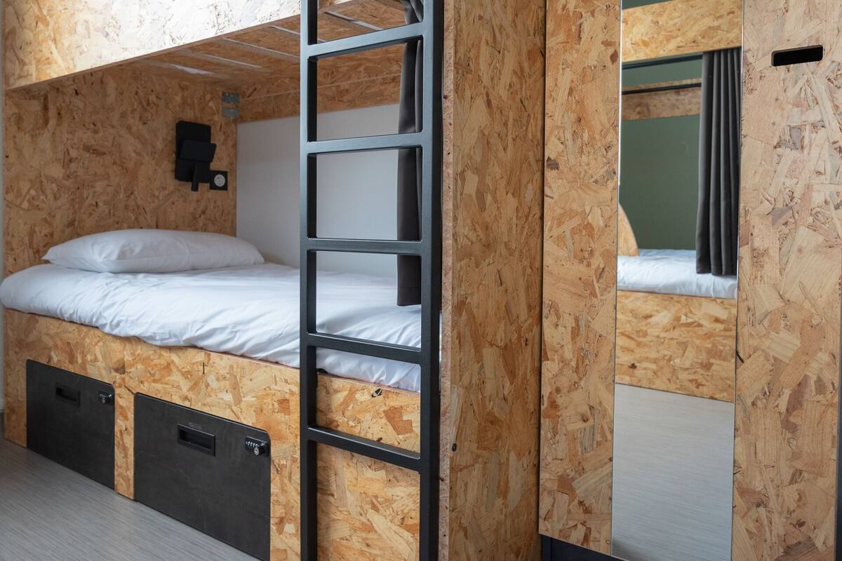 A bunk bed room with a ladder, a small black heater, and a window with curtains.