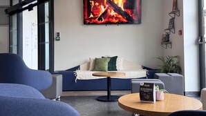 A modern lounge area with a sofa, round table, and a large fire-themed artwork on the wall. - Auberge de jeunesse HI Clermont-Ferrand (Clermont-Ferrand)