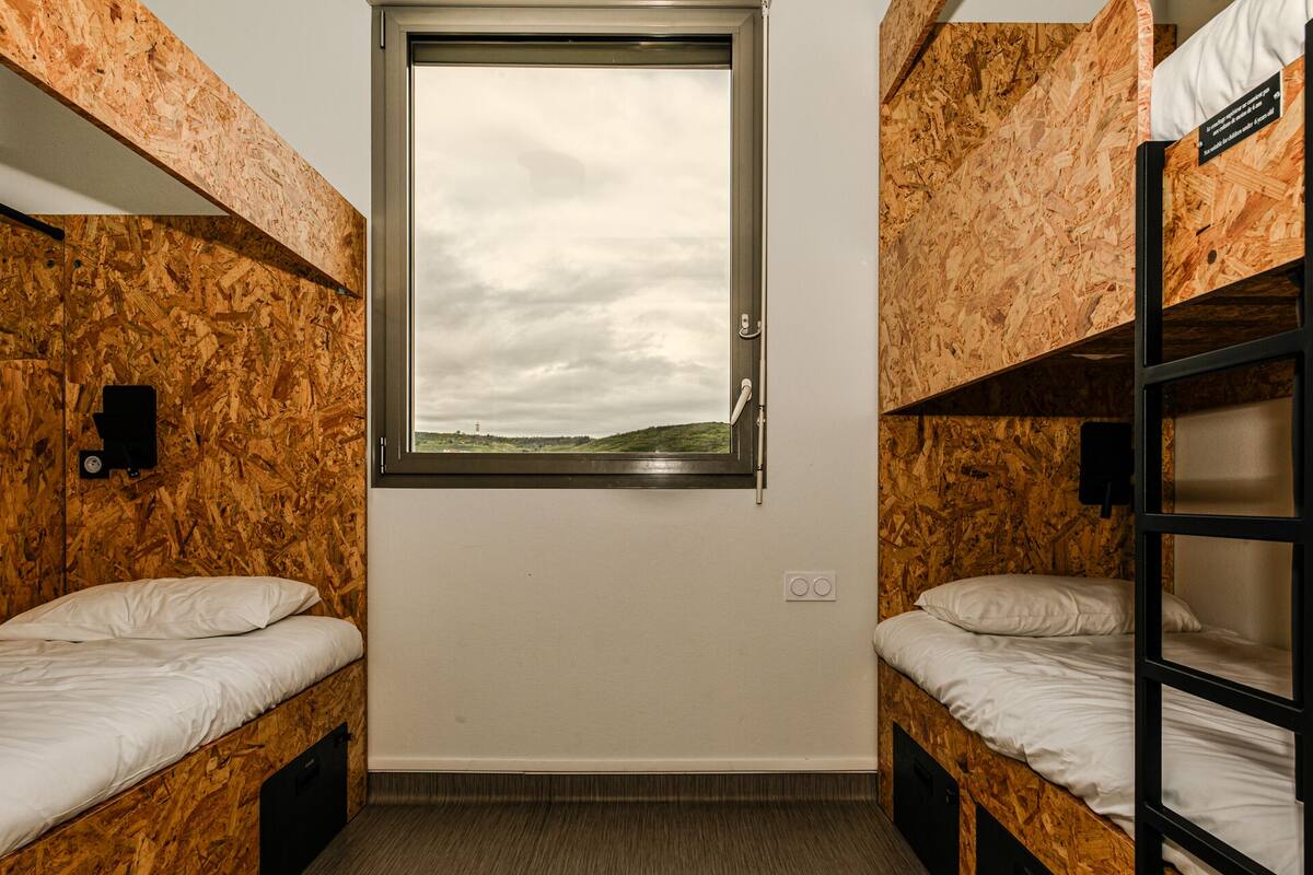 A compact room with bunk beds, a window with a view of a cloudy sky, and a small wall-mounted light fixture.