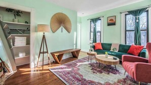 Un salon avec un canapé vert, un banc en bois, une table basse ronde et un grand tapis à motifs.