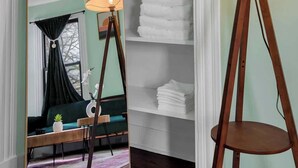 Une pièce dotée d’un grand miroir qui reflète un coin salon accueillant, d’un lampadaire en bois et d’une étagère où sont pliées des serviettes.