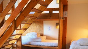 Een slaapkamer in een loft met een houten trap, een bed met wit beddengoed en een klein nachtkastje.