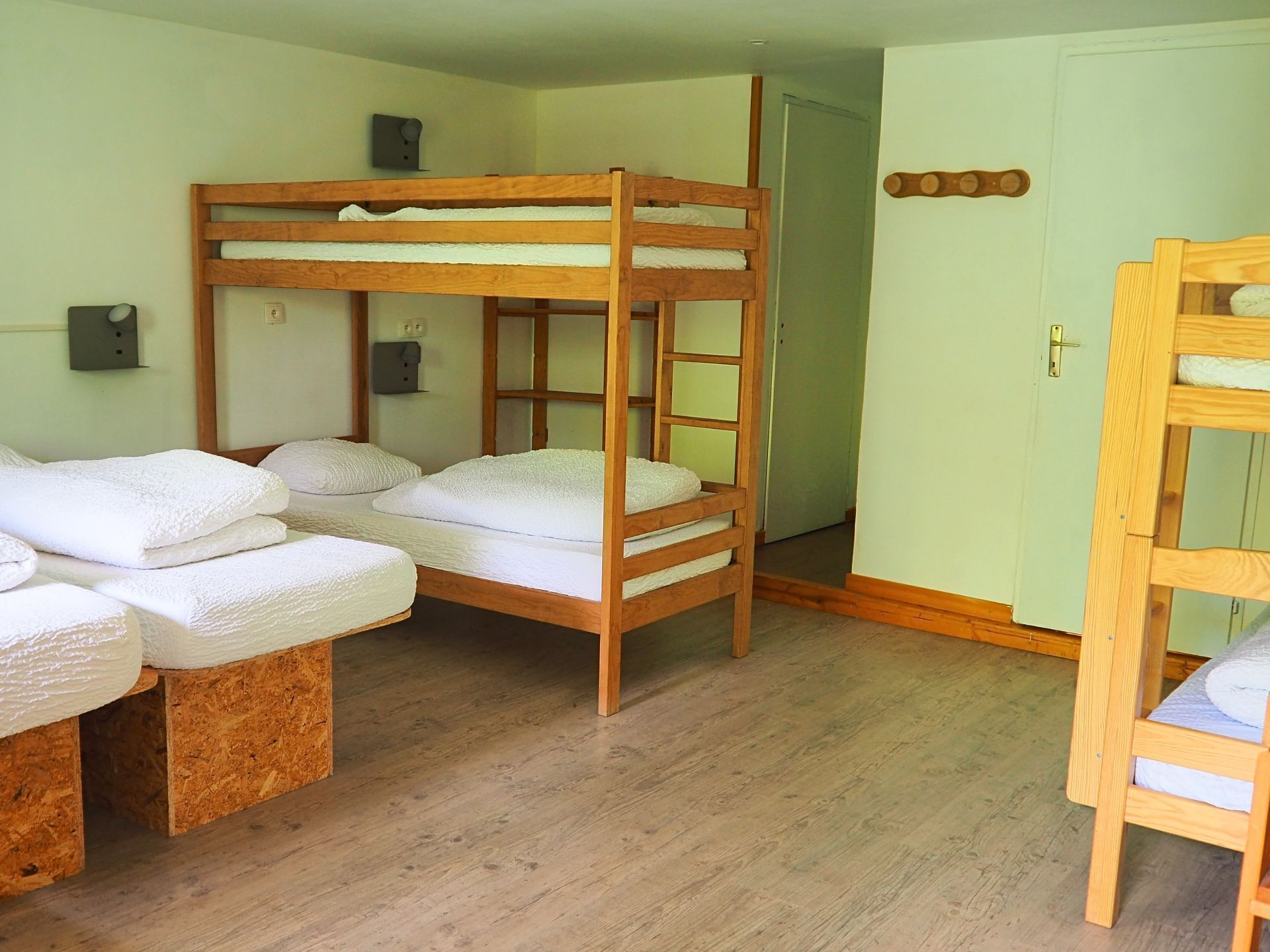 A room with bunk beds, wooden flooring, and a door.