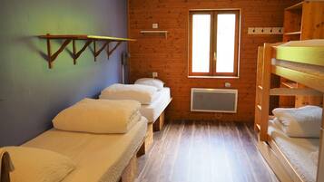 Een kleine, knusse kamer met twee eenpersoonsbedden, een houten stapelbed, een raam met daglicht en een wandradiator.