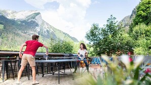 Twee personen spelen tafeltennis buiten, met een bergachtige achtergrond.