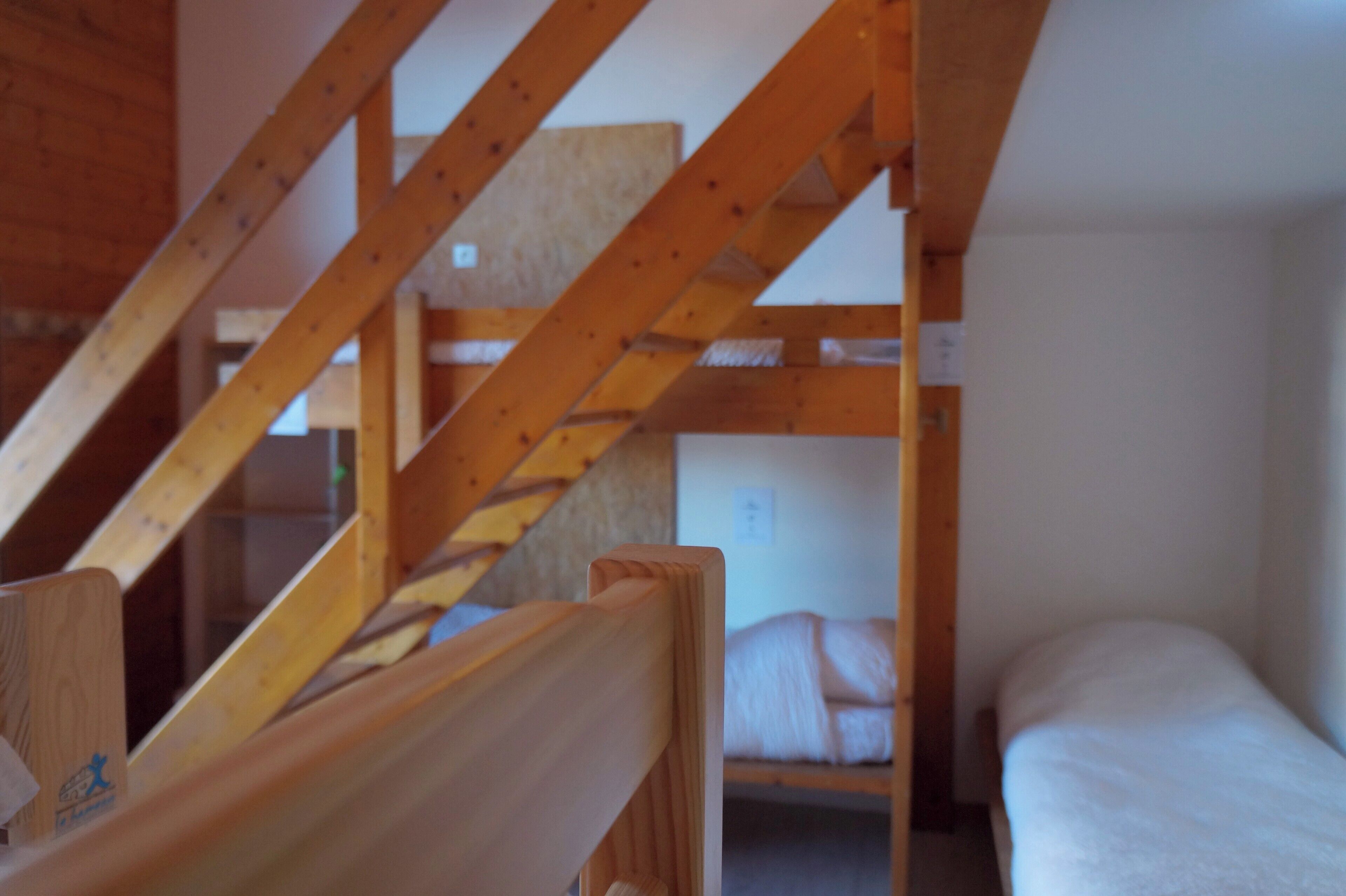 A wooden staircase leading to a bunk bed room with a white wall and a small window.