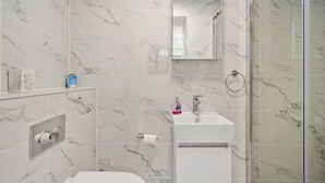 Un baño moderno con baldosas de mármol, un lavamanos blanco, cabina de ducha con mampara de vidrio y un espejo sobre el lavamanos.