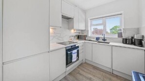 Una cocina moderna con armarios blancos, horno integrado, microondas y ventana que proporciona luz natural.
