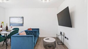 Una sala de estar moderna con un sofá azul, una mesa redonda de centro y un televisor de pantalla plana montado en la pared.