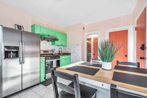 Une cuisine moderne avec un réfrigérateur en acier inoxydable, des armoires vertes, une table à manger en bois et une plante en pot.