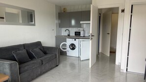 A compact living space with a grey sofa, a washing machine, a microwave, and a small kitchen area. - Nice place with sea and swimming pool (Saint-Raphaël)