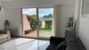 A living room with a sliding glass door leading to a balcony, a sofa, a fan, and a small table with a lamp. - Nice place with sea and swimming pool (Saint-Raphaël)