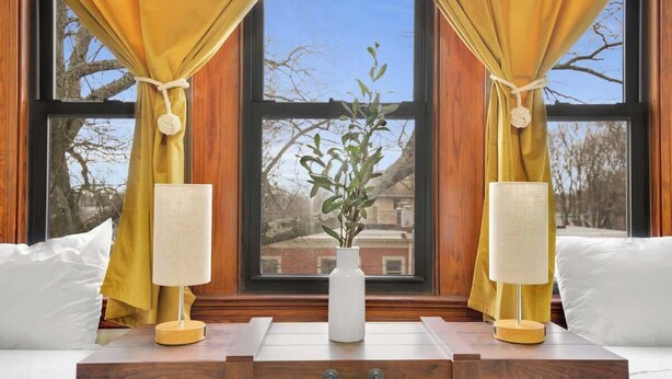 A room with a large window, wooden furniture, and a vase with a plant.