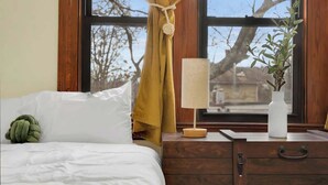 A room with a bed, a nightstand with a lamp, a window with curtains, and a radiator.