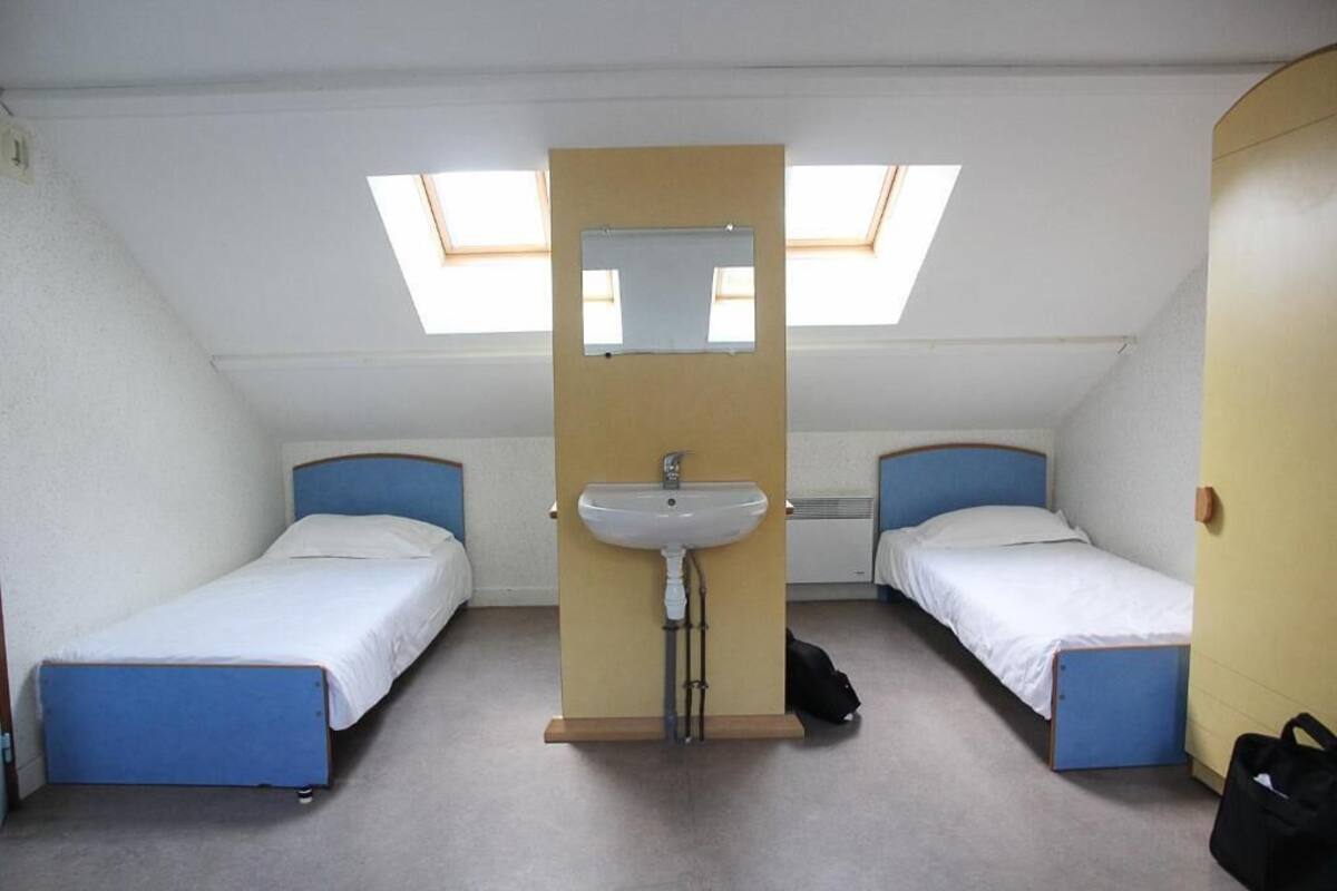 Una habitación pequeña y compacta con dos camas individuales, un lavamanos central y tragaluces.