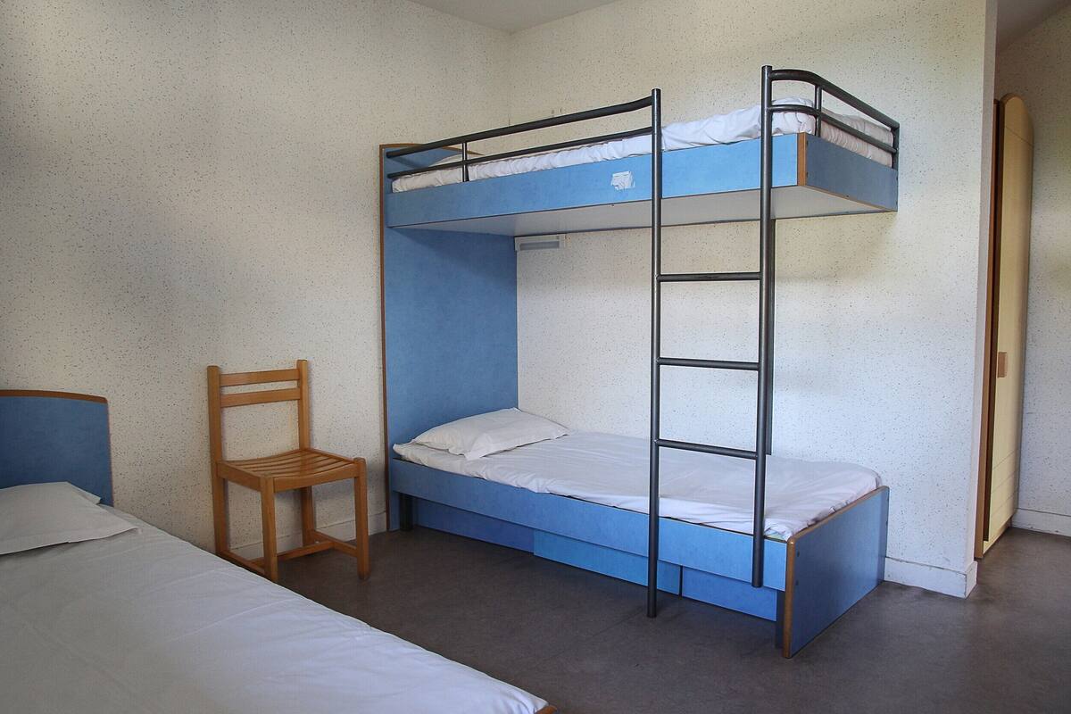 Dormitorio con literas, una silla de madera y un escritorio.