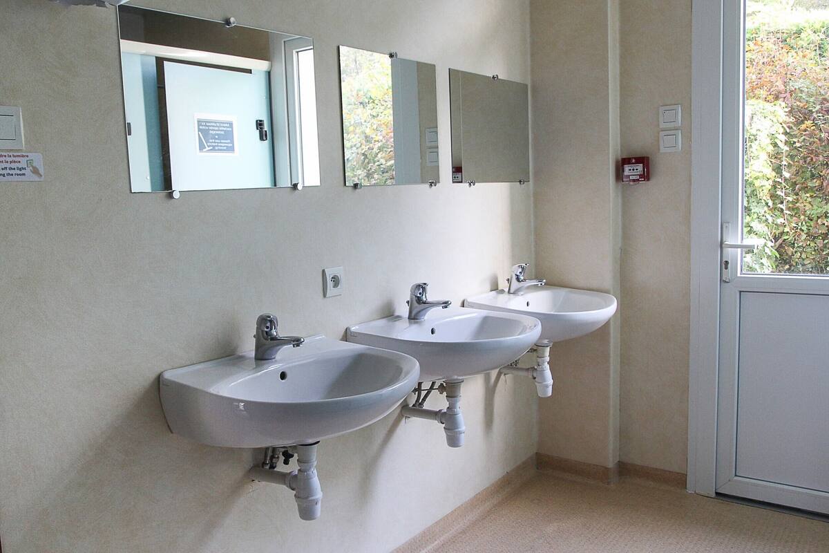 Baño con tres lavamanos, un espejo sobre cada uno, y una puerta con un letrero.