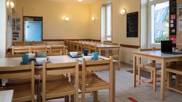 A dining area with multiple wooden tables and chairs, a blue door, and a window with a view of the outside.
