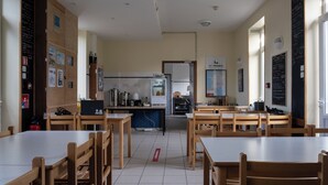 Un comedor amplio con mesas y sillas de madera, una cocina al fondo y un menú en una pizarra en la pared.