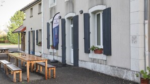 Un edificio de fachada blanca, con contraventanas oscuras y una mesa de madera con bancos en el exterior.