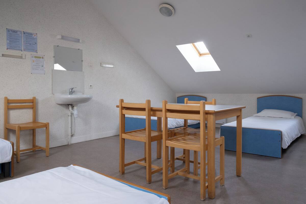 Un dormitorio con tragaluz, un lavabo, dos camas y una mesa con sillas.