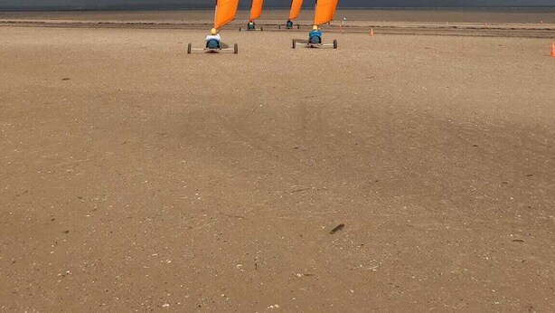 Una playa con tres veleros naranjas y un cielo nublado.