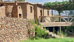 Un edificio rústico de piedra con una terraza de madera que da a una masa de agua.