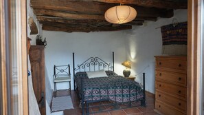 A bedroom with a bed, a chair, a dresser, and a hanging light fixture.