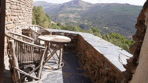 Un espacio de estar al aire libre rústico, con paredes de piedra y vistas a un paisaje montañoso.