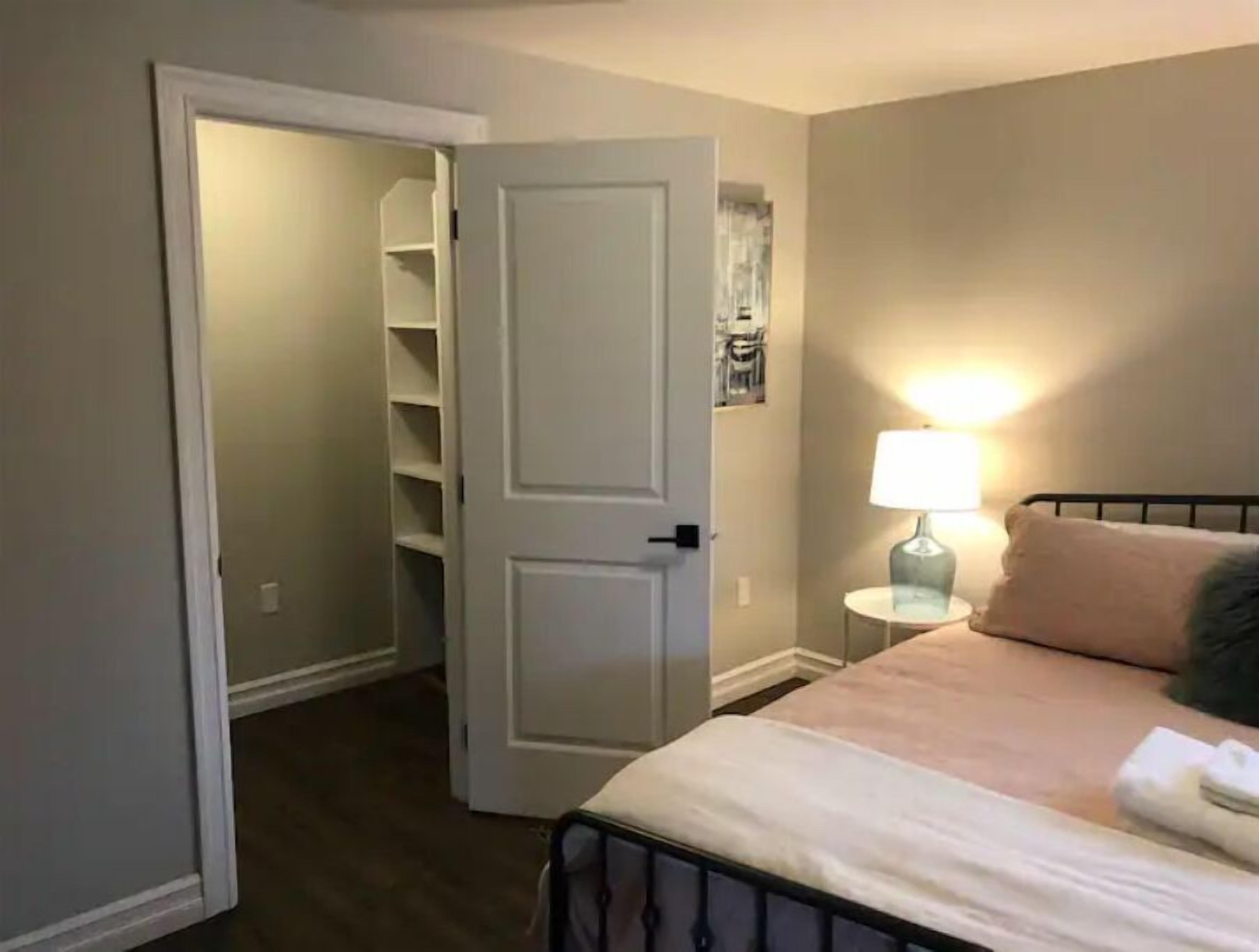 A bedroom with a bed, a bedside lamp, and a closet with shelves.