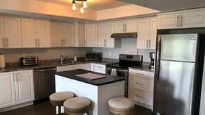 Una cocina moderna con gabinetes blancos, un refrigerador de acero inoxidable, un microondas y una isla central con taburetes.