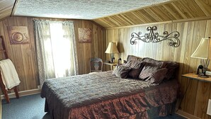 A bedroom with a large bed, wooden walls, a decorative headboard, a nightstand with a lamp, and a window with curtains.