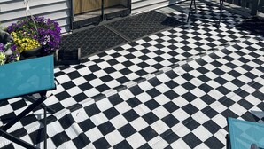 A house with a black and white checkered patio, a wooden door, and a window with a yellow frame.