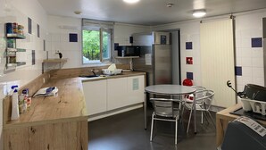Una cocina moderna con armarios blancos, un refrigerador de acero inoxidable, una ventana con vistas a zonas verdes y un comedor con una mesa redonda y sillas.